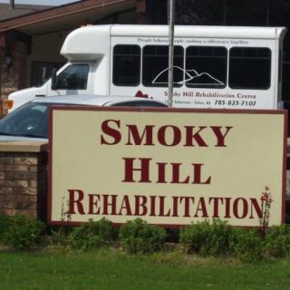A sign for Smoky Hill Rehabilitation in front of a building and a van.