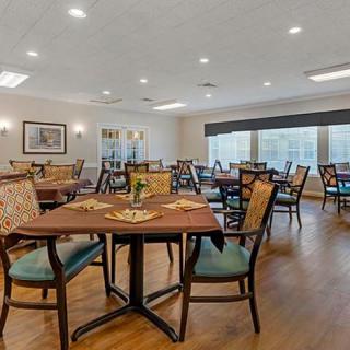 A spacious dining area with neatly arranged tables and chairs, featuring warm lighting and a wooden floor.
