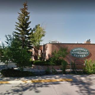 A brick building surrounded by trees with a visible sign and adjacent street.