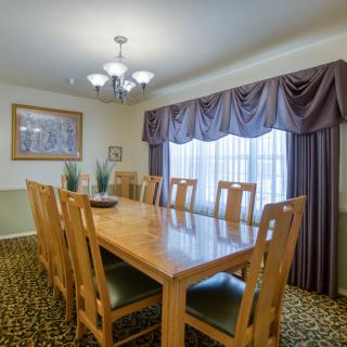 A dining room with a large wooden table, surrounded by chairs and lit by a chandelier.