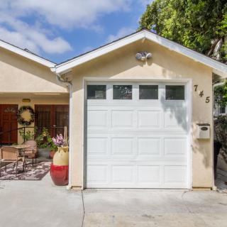 A cozy house with a single-car garage and a small outdoor seating area on a sunny day.