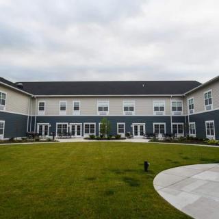 A modern two-story building with a courtyard and well-maintained lawn under a cloudy sky.