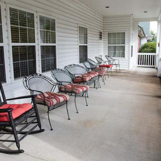 A spacious porch with multiple chairs lined up along the wall, including a rocking chair.