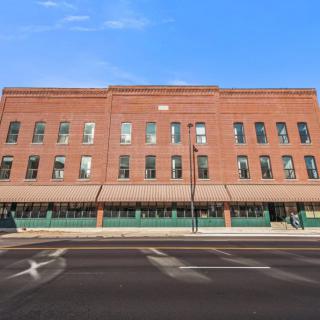 A large brick building with multiple windows, situated alongside a street under a clear blue sky.