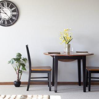 A minimalist dining area featuring a wooden table and chairs,
complemented by a wall clock, indoor plant, and vase of flowers.