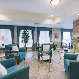 A modern living room with teal armchairs, glass coffee tables, and large windows with curtains.