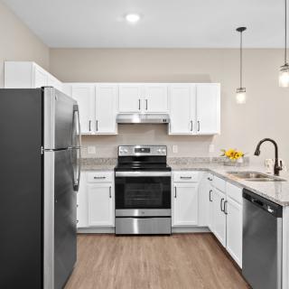 A modern kitchen with white cabinetry and stainless steel appliances, featuring a refrigerator, oven, and dishwasher.