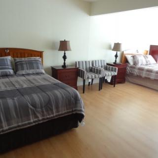 A spacious bedroom featuring two beds with striped bedding, nightstands, lamps, and chairs on a hardwood floor.