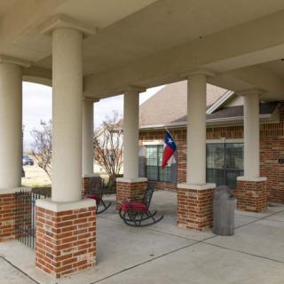 A covered patio with brick columns features rocking chairs and a Texas flag.