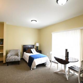 A cozy bedroom with a single bed, chair, small table, and lamp by the window.