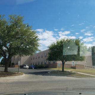 A view of a building surrounded by trees under a partly cloudy sky.