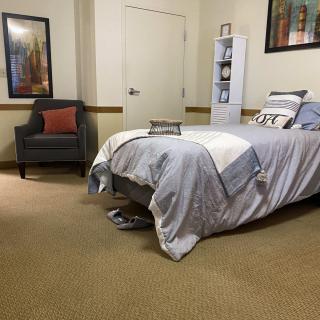A cozy bedroom with a neatly made bed, an armchair with a cushion, and framed artwork on the walls.