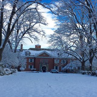A grand mansion surrounded by snow-laden trees under a clear blue sky.