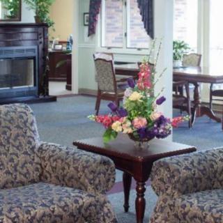 A cozy living room with patterned chairs and a small table topped with a floral arrangement, set near a fireplace.