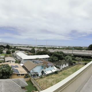 Aerial view of a suburban neighborhood with houses and a highway in the distance under a cloudy sky.
