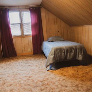 A cozy attic bedroom with wood paneling, a single bed, and purple curtains.