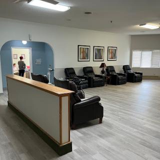 A spacious waiting area featuring comfortable recliners and a reception desk, adorned with artwork on the walls.