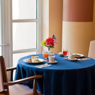 A cozy breakfast setup on a table with a blue tablecloth, decorated with flowers and morning light streaming in through the window.