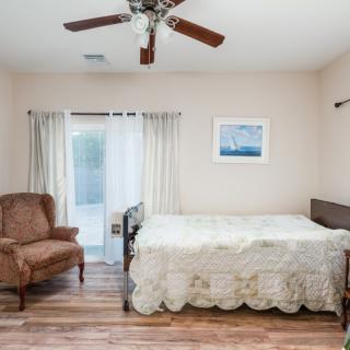 A cozy bedroom with a bed, armchair, ceiling fan, and curtains by the window.