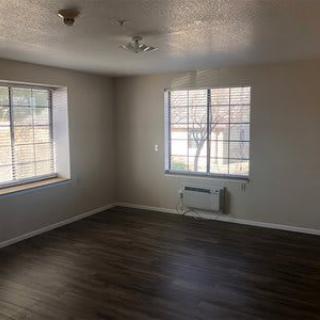 An empty room with hardwood flooring and large windows.