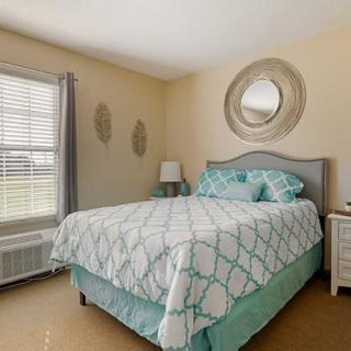 A cozy bedroom with a neatly made bed, decorative mirror, and a bedside lamp.