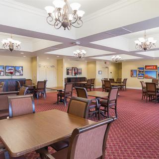 A spacious dining room with elegant chandeliers, wooden tables, and a red carpeted floor.