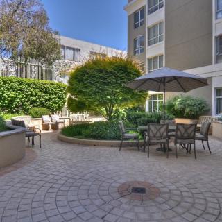 A peaceful courtyard featuring outdoor seating, greenery, and an umbrella for shade.