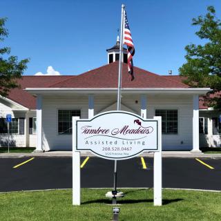 A building with a sign reading 'Carefree Meadows Assisted Living' and an American flag in front.