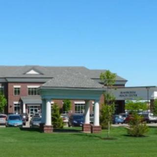 A hospital building with parked cars and landscaped surroundings on a clear day.