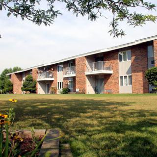 A brick apartment building with balconies and a grassy lawn in the foreground.
