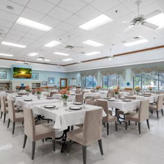 A spacious and elegantly set dining area with multiple tables and chairs, featuring large windows and ceiling lights.
