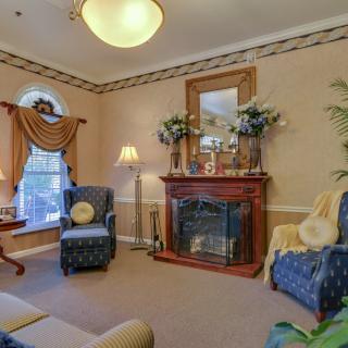A traditional living room featuring a fireplace, two blue armchairs, elegant drapes, and decorative elements such as a mirror and plants.