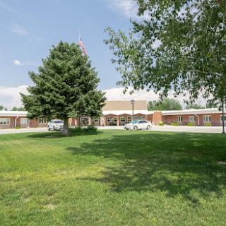 A serene view of a building surrounded by lush green grass and trees under a clear sky.