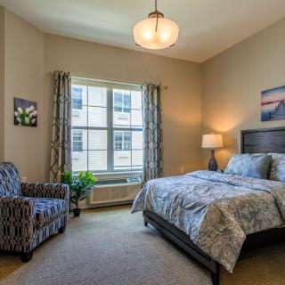 A cozy bedroom with modern decor, featuring a bed, chair, lamp, and window.