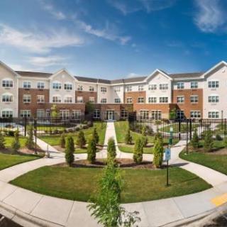 A modern apartment complex with well-maintained landscaping and clear pathways under a partly cloudy sky.