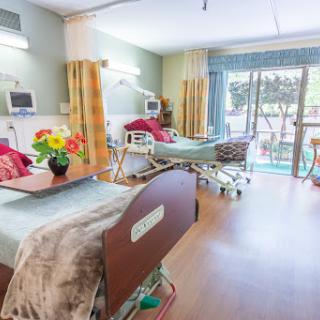 A well-lit hospital patient room featuring two beds, decorative flowers, and a view outside.
