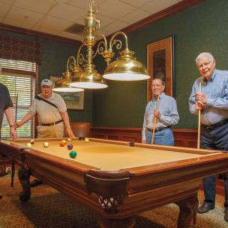 A group of people enjoying a game of billiards in a warmly lit room.