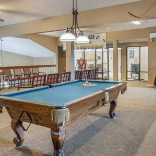 A well-lit game room featuring a classic pool table and comfortable seating.