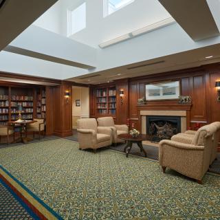 A cozy library room featuring armchairs, a fireplace, and bookshelves filled with books.
