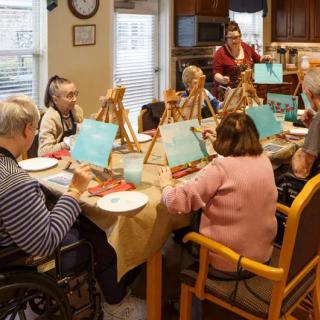 A group of seniors engaging in a painting class, creating art and enjoying a communal activity indoors.
