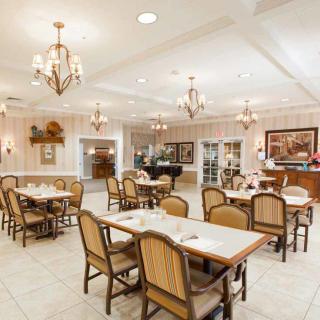 A spacious and elegantly decorated dining room with multiple tables and chairs, illuminated by chandeliers.