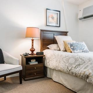 A cozy bedroom featuring a neatly made bed, a wooden nightstand with a lamp, and a decorative chair.