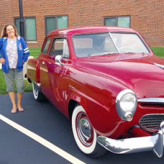 A woman stands next to a beautiful red classic car, showcasing the charm of vintage automobiles.