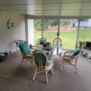 A cozy sunroom with rattan furniture and a glass table overlooking a garden.