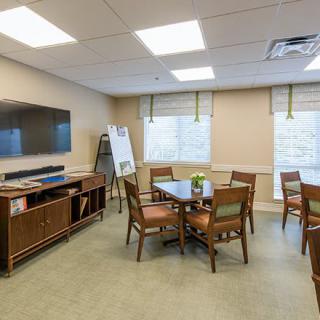 A well-lit conference room with a table, chairs, a television, and windows.
