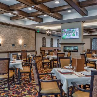 A cozy restaurant dining area with neatly arranged tables and chairs, featuring elegant interior design elements like ceiling beams and wall lighting.