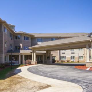 A modern residential building with a covered entrance and circular driveway under a clear blue sky.