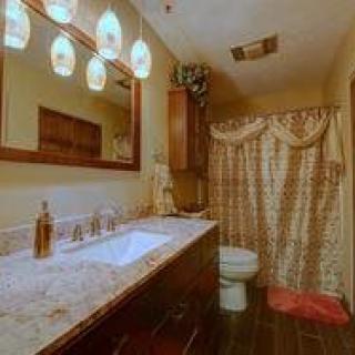 A cozy bathroom featuring a granite countertop with a vanity and sink, well-lit by elegant pendant lights above. The shower is adorned with an ornate curtain, complementing the warm-toned decor.