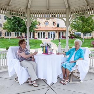 Two seniors enjoying a conversation in a gazebo setting outdoors.
