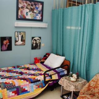 A cozy bedroom with a colorful patchwork quilt, adorned with photos on the walls and light blue curtains.